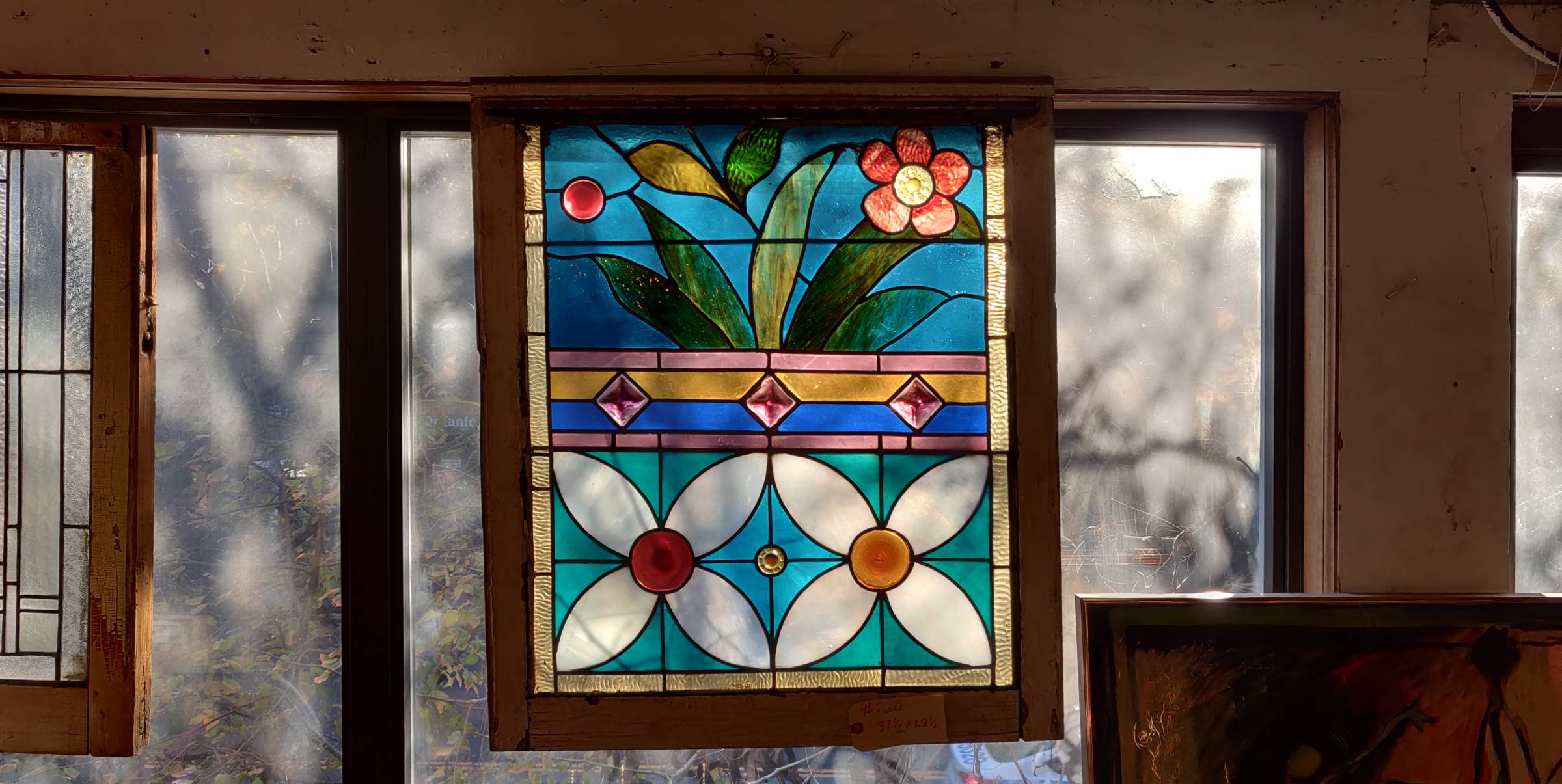 Winter sunlight shines through a stained glass panel in an antique shop. The top half of the panel shows live flowers, the bottom a geometric flower motif.